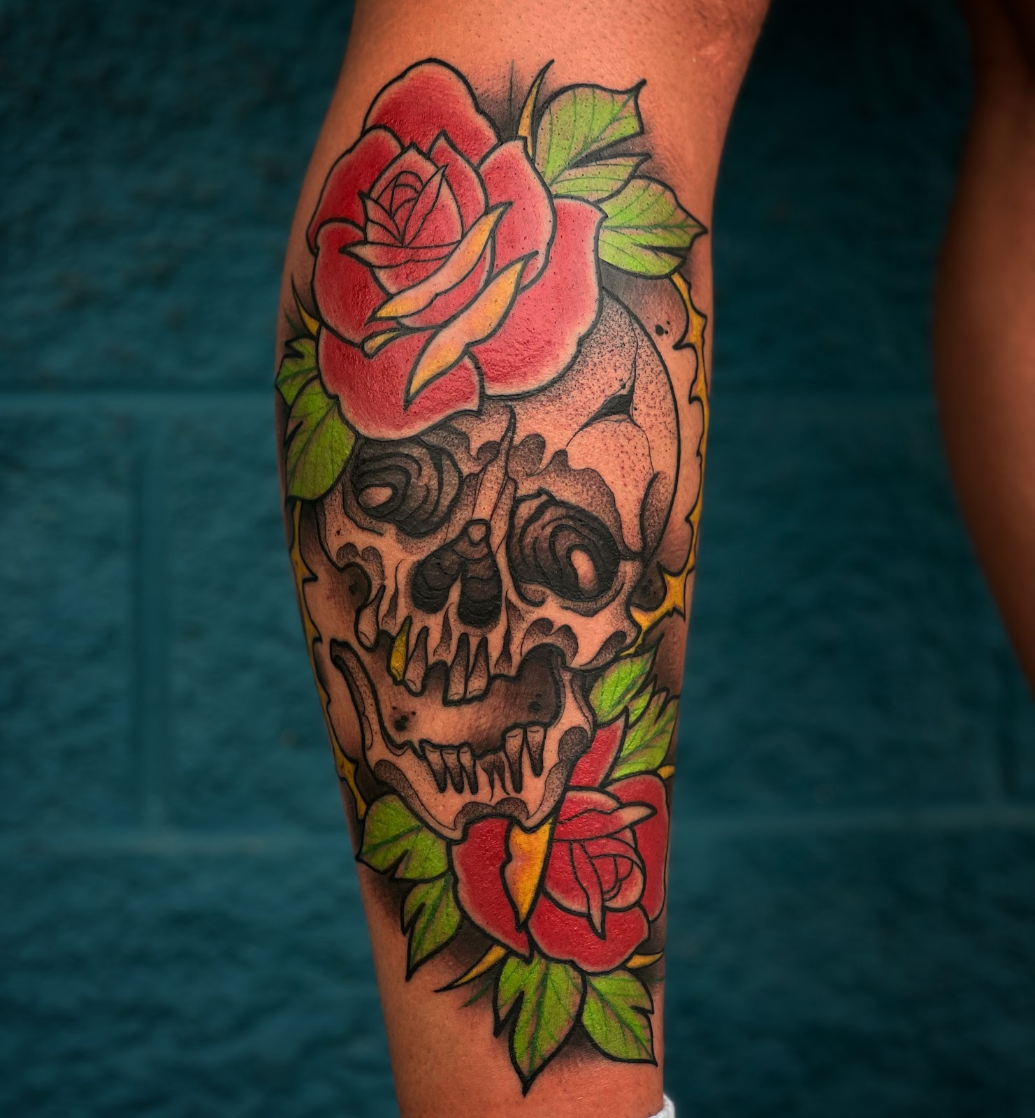Color tattoo of a skull wrapped in red roses and green leaves on a calf