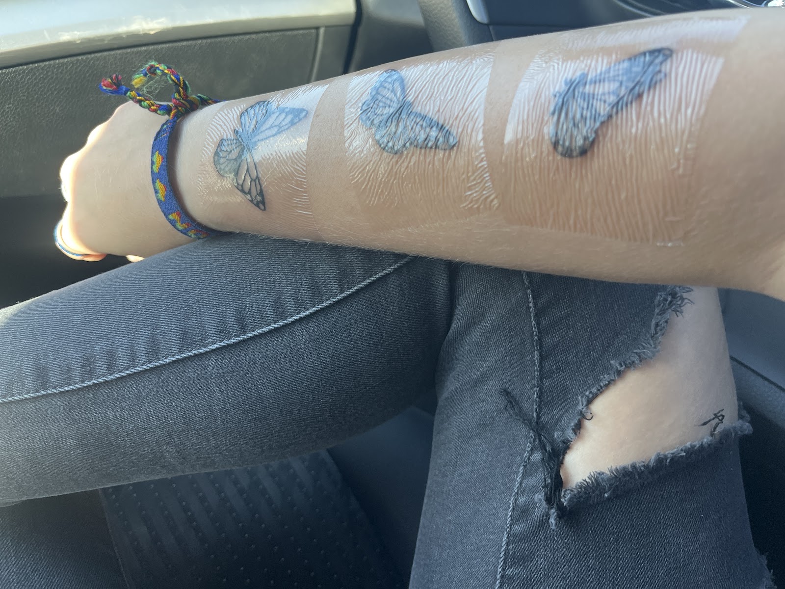 Three fresh butterfly tattoos along a forearm, wrapped in healing film