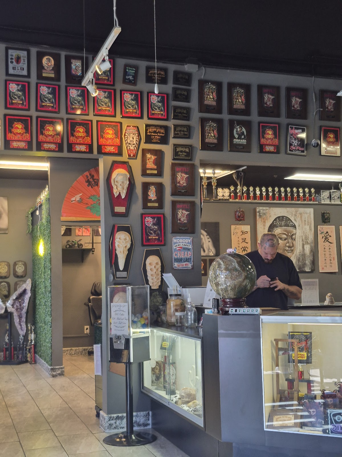 Shop walls covered in framed convention award plaques and sculpted coffin awards, with a shelf of trophies above the counter