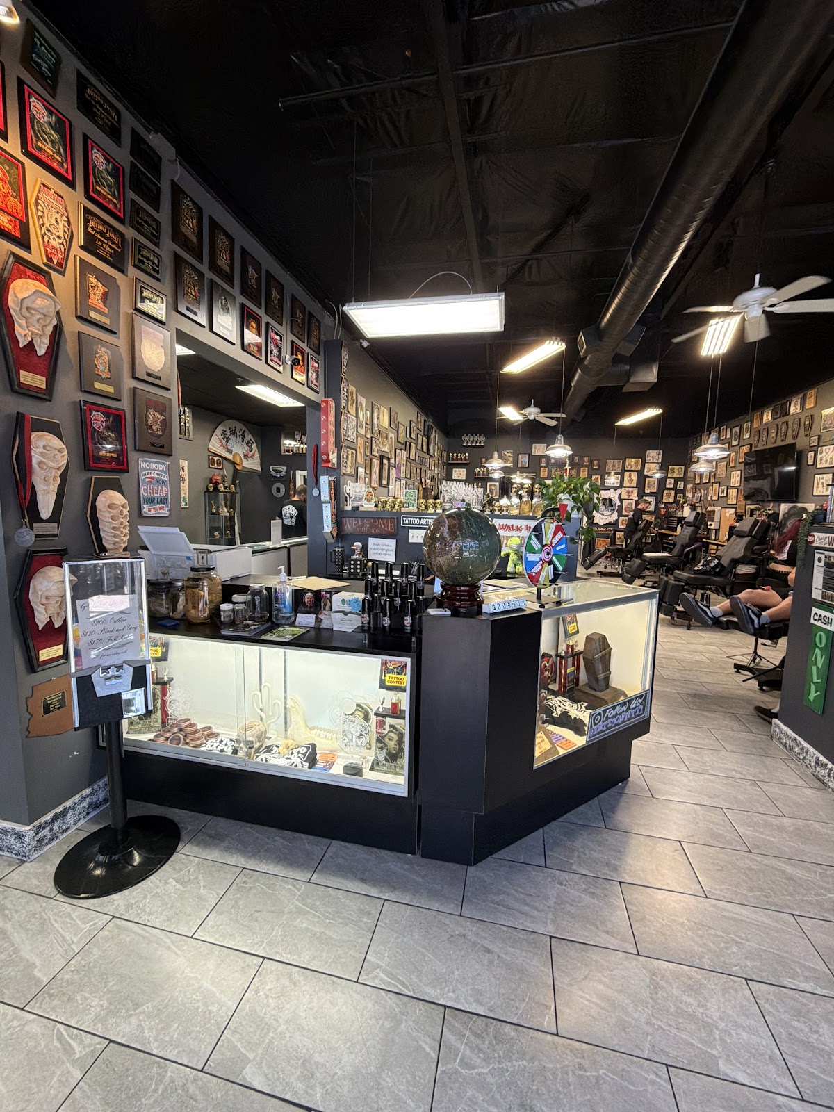 Front counter with glass display cases, the prize wheel, and artists tattooing in the background