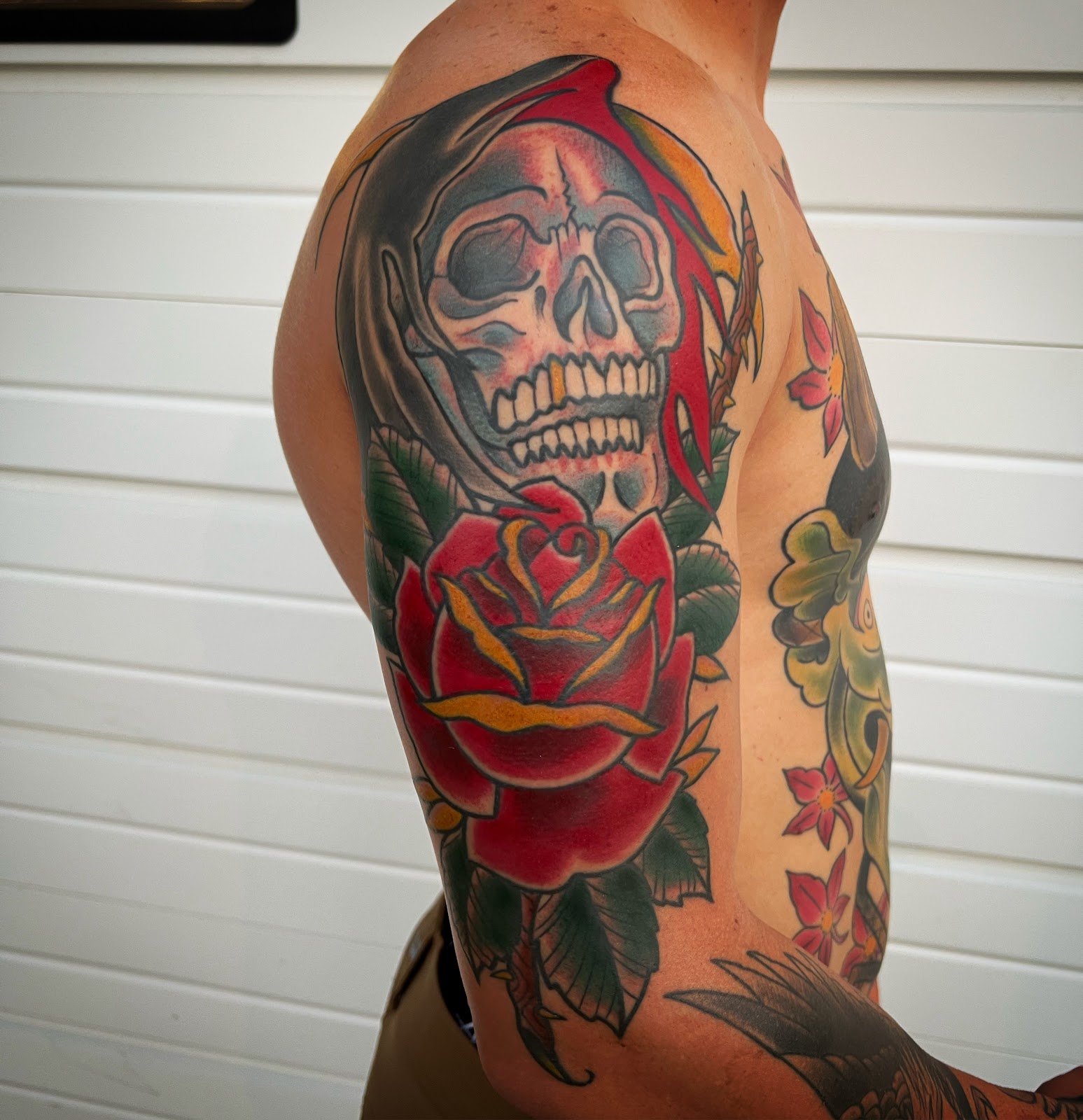 American traditional reaper skull with a red rose covering a shoulder