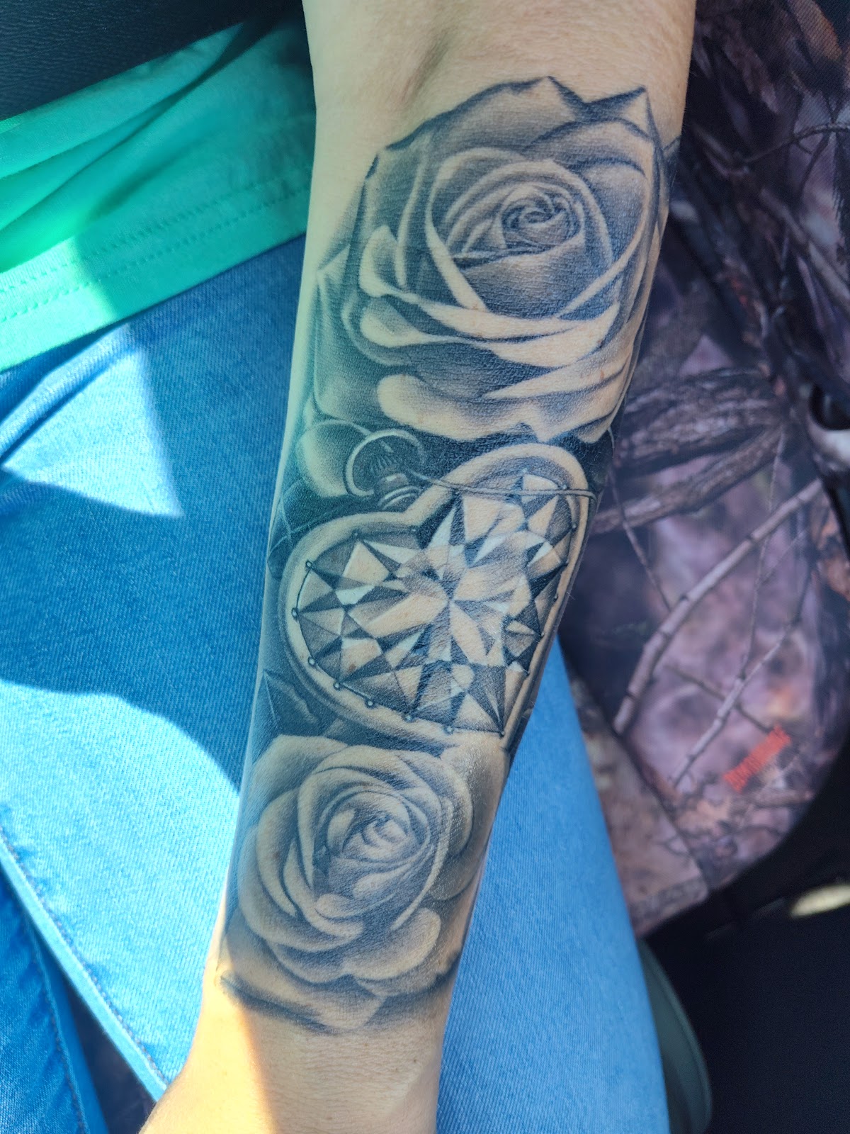 Black and grey forearm piece: two roses around a heart-cut gem